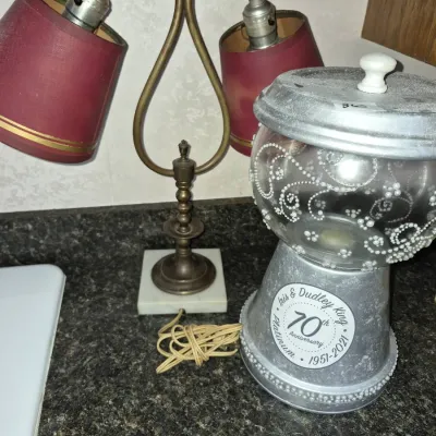 Sale Photo Thumbnail #628: Vintage brass two-light desk lamp with red shades alongside a customized gumball machine commemorating a 70th platinum wedding anniversary.