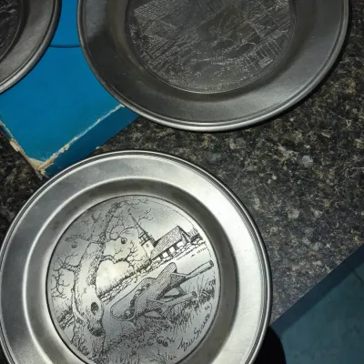 Sale Photo Thumbnail #692: Set of Eric Sloane etched pewter collector plates featuring rural landscape designs, displayed alongside an original box.