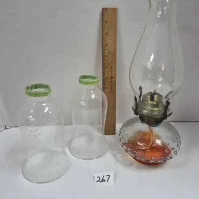 Sale Photo Thumbnail #455: Vintage glass oil lamp with hobnail base alongside two clear hurricane lamp chimneys featuring green rims and etched details.
