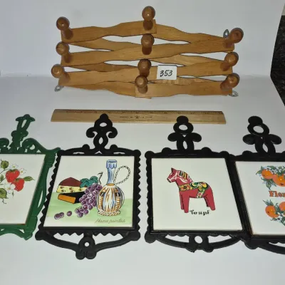 Sale Photo Thumbnail #616: Collection of four vintage cast iron trivets with decorative ceramic tile inserts and an accordion-style wooden wall rack.
