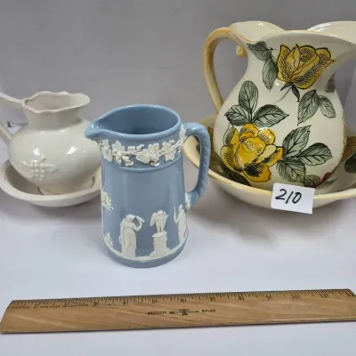 Sale Photo Thumbnail #360: Collection of decorative pitchers, including a blue Jasperware pitcher, a floral pitcher with matching washbasin bowl, and a small cream-colored pitcher and basin set.