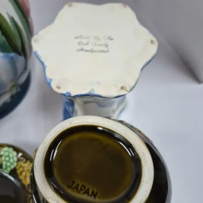 Sale Photo Thumbnail #227: Underside maker's marks on vintage ceramics, including a dark green glazed piece stamped "JAPAN" and a hand-painted floral vase.