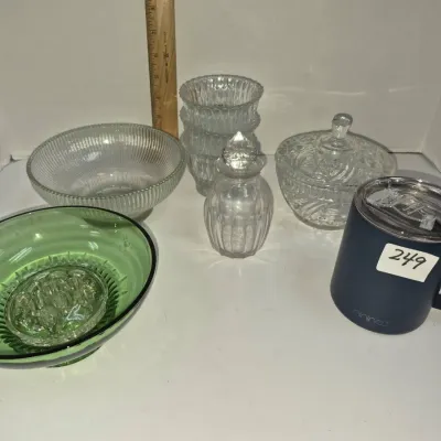 Sale Photo Thumbnail #424: Collection of assorted glassware including a green depression glass bowl with a glass flower frog, ribbed clear glass bowls, a perfume bottle, a covered candy dish, and a modern navy blue insulated travel mug.