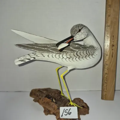 Sale Photo Thumbnail #272: Hand-carved and painted wooden shorebird sculpture mounted on a natural driftwood base, depicted holding a small shell in its beak.