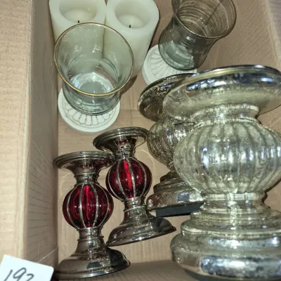 Sale Photo Thumbnail #331: Cardboard box packed with various candle holders, including silver-tone mercury glass pedestals, red glass and metal candleholders, clear glass hurricanes, and pillar candles.