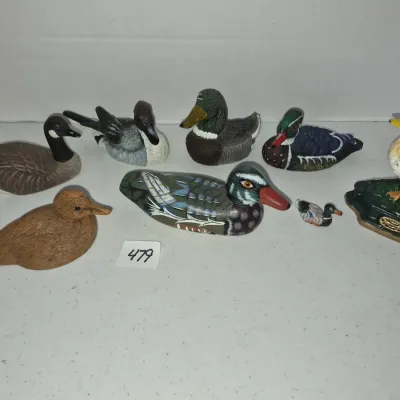 Sale Photo Thumbnail #823: Collection of eight small waterfowl and duck figurines, including hand-painted wooden decoys, resin figures, and cast iron pieces in various species and sizes.