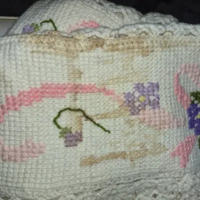 Sale Photo Thumbnail #83: Handmade crocheted item featuring embroidered floral motifs with ribbons, showing visible staining along the fabric.