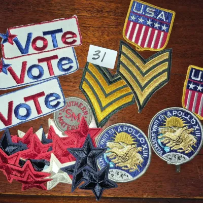 Sale Photo Thumbnail #48: Collection of vintage embroidered patches featuring political 'Vote' tags, Apollo XIII mission emblems, U.S. flag shields, military chevrons, and red, white, and blue star shapes.