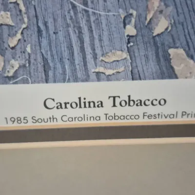 Sale Photo Thumbnail #477: Detail view of a framed art print titled 'Carolina Tobacco,' produced for the 1985 South Carolina Tobacco Festival.