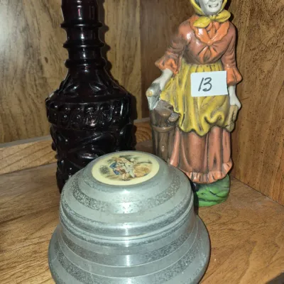 Sale Photo Thumbnail #21: Collection of vintage decor items, including a dark red pressed glass bottle, a hand-painted figurine of an elderly woman, and a metallic trinket box with an inlaid image.