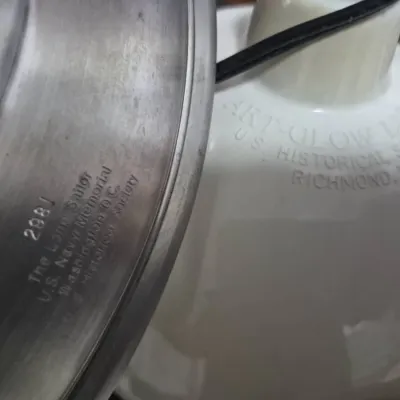 Sale Photo Thumbnail #23: Numbered commemorative pewter plate featuring 'The Lone Sailor' from the U.S. Navy Memorial, alongside a white ceramic lamp component embossed with 'Art-Glow Lite U.S. Historical Society, Richmond, VA'.