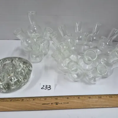 Sale Photo Thumbnail #400: Collection of vintage clear glass flower frogs, including a solid dome style and multi-spout cluster vases, displayed alongside a ruler for scale.