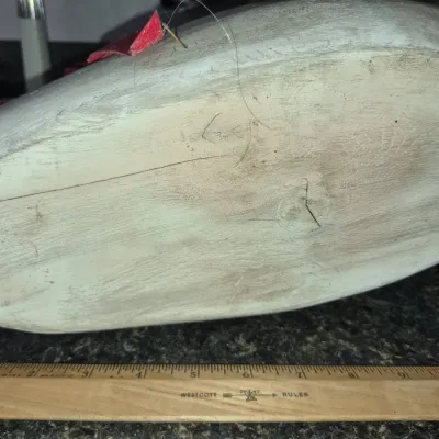 Sale Photo Thumbnail #539: Underside of a carved wooden duck decoy next to a Westcott wooden ruler, showing a weathered paint finish and a crack along the wood grain.