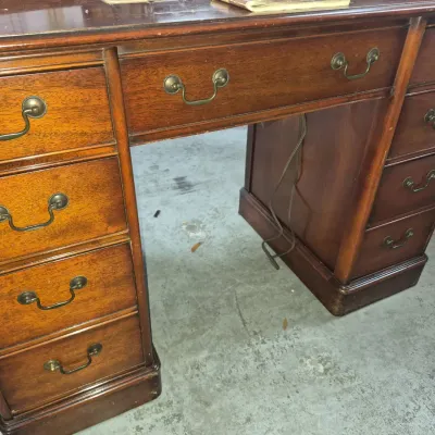 Sale Photo Thumbnail #54: Traditional mahogany pedestal desk featuring brass bail handles, multiple drawers for storage, and visible wear along the base.