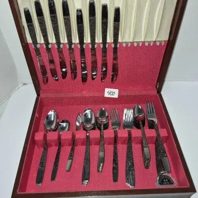 Sale Photo Thumbnail #703: Vintage stainless steel flatware set featuring detailed handles, housed in a wooden storage chest lined with red felt.
