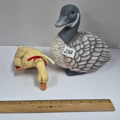 Sale Photo Thumbnail #408: Pair of decorative bird figurines, including a ceramic Canada goose decoy and a small yellow duck tied with ribbons, displayed alongside a wooden ruler for scale.
