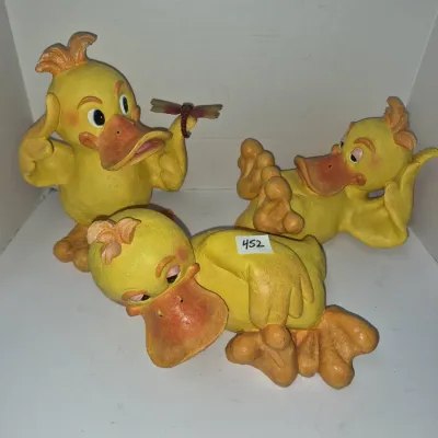 Sale Photo Thumbnail #782: Set of three whimsical yellow duck resin figurines in various playful poses, including one holding a dragonfly.