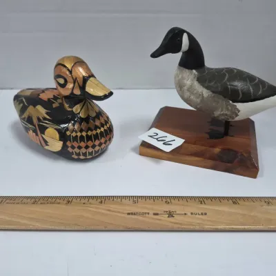 Sale Photo Thumbnail #453: Pair of small bird figurines, including a carved wooden Canada goose on a display base and a lacquered decorative duck with metallic accents.