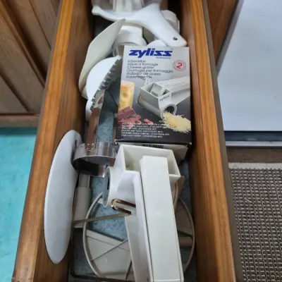 Sale Photo Thumbnail #683: Open wooden kitchen drawer filled with assorted vintage kitchen gadgets, including a Zyliss cheese grater in its original box and a manual citrus juicer.