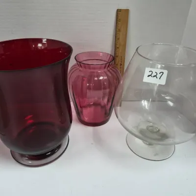 Sale Photo Thumbnail #391: Collection of three glass vases, including a large ruby red hurricane-style vase, a small ribbed amethyst vase, and a oversized clear glass footed snifter vase.