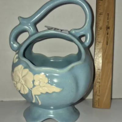 Sale Photo Thumbnail #265: Vintage light blue pottery basket vase featuring raised cream floral accents and an ornate handle, standing approximately 8 inches tall.