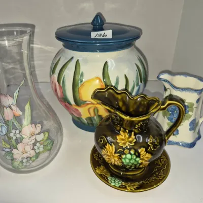 Sale Photo Thumbnail #226: Collection of decorative ceramic and glass tableware, including a lidded floral jar, a hand-painted glass vase, and two ceramic pitchers.