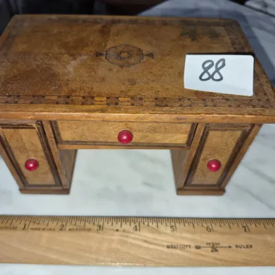 Sale Photo Thumbnail #141: Miniature wooden desk-form trinket box with marquetry inlay details and small red knobs, measuring under six inches long.