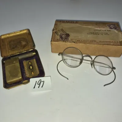 Sale Photo Thumbnail #337: Vintage wire-rimmed spectacles with curved ear pieces and original mailing box, paired with a brass safety razor set in a fitted metal case.