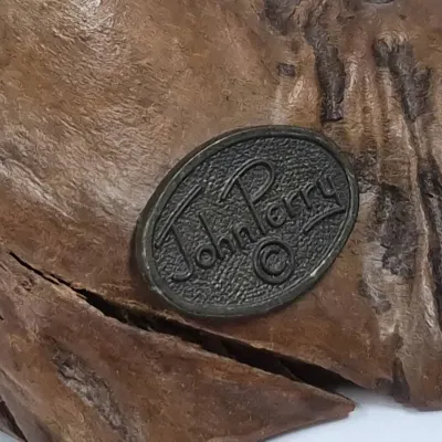 Sale Photo Thumbnail #388: Detail shot of an oval John Perry maker's mark medallion embedded on a burl wood sculpture base.