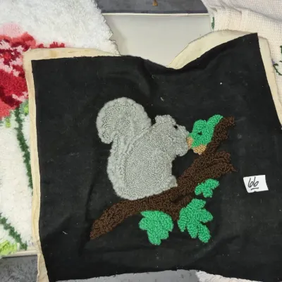 Sale Photo Thumbnail #99: Selection of handcrafted textiles, including latch hook squirrel and rose pillow tops alongside a needlepoint piece.