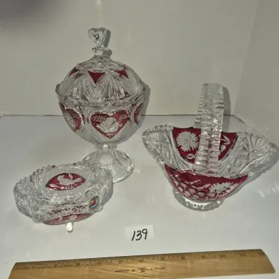 Sale Photo Thumbnail #231: Three-piece collection of ruby stain cut glass decorative glassware, including a footed lidded candy dish, a handled basket, and a lidded trinket box.