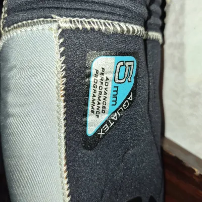 Sale Photo Thumbnail #320: Close-up detail of an Aquatex 5mm neoprene wetsuit showing heavy-duty flatlock stitching and brand labeling in used condition.