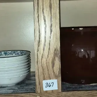 Sale Photo Thumbnail #634: Collection of kitchenware stored in a cabinet, including stacks of ceramic plates, floral pattern bowls, a dark brown glazed bean pot, and woven wooden bowls.