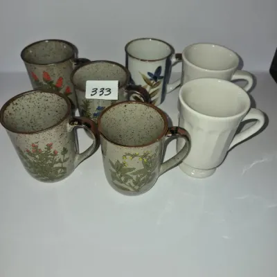 Sale Photo Thumbnail #581: Collection of seven stoneware and ceramic mugs, including speckled stoneware mugs with floral motifs and white paneled mugs.