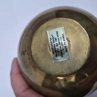 Sale Photo Thumbnail #412: Underside of a brass object featuring an original maker's label reading 'Handcrafted for The MASTER Teacher', made in Korea.