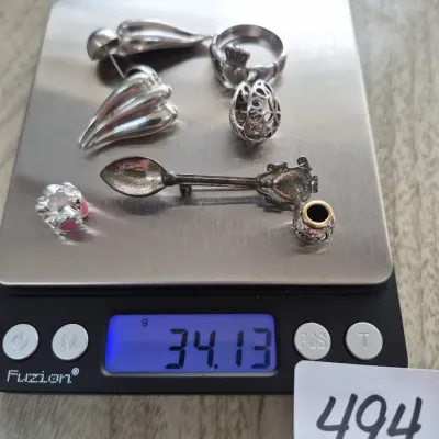 Sale Photo Thumbnail #848: Assorted sterling silver jewelry lot including a Claddagh ring, spoon pin brooch, beads, and clip-on earrings, weighing 34.13 grams on a digital scale.