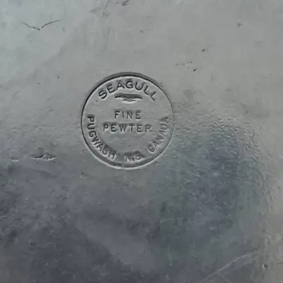 Sale Photo Thumbnail #708: Close-up of a maker's mark reading "Seagull Fine Pewter, Pugwash N.S. Canada" stamped on a metal surface.
