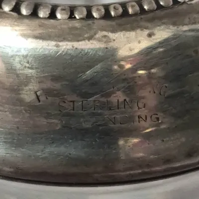 Sale Photo Thumbnail #911: Close-up detail of a silver item's hallmark, stamped STERLING along a beaded rim.