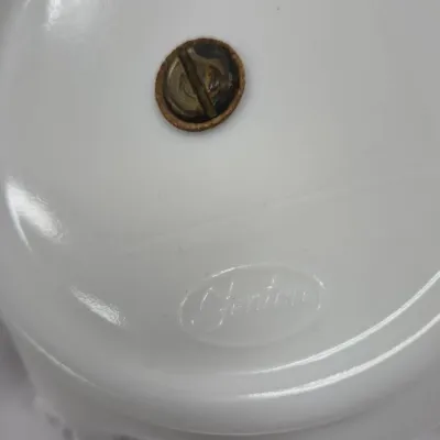 Sale Photo Thumbnail #353: Underside of a vintage Fenton white milk glass piece featuring an embossed logo mark and a central metal screw attachment.