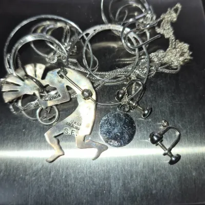 Sale Photo Thumbnail #854: Assortment of sterling silver jewelry on a digital scale, including hoop earrings, chains, screw-back earrings, and a Kokopelli pin hallmarked 12KGF STERLING S.E.