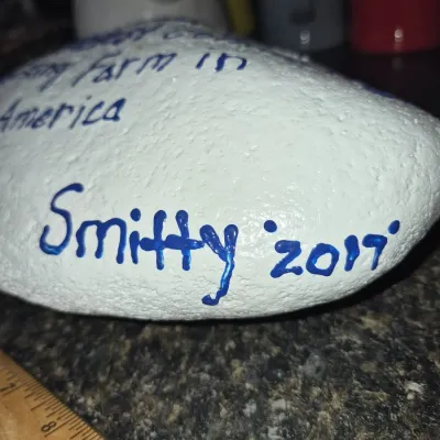 Sale Photo Thumbnail #553: Hand-painted souvenir river rock coated in white paint with blue lettering, signed 'Smitty '2017'.