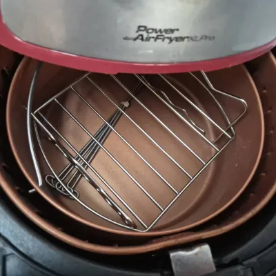 Sale Photo Thumbnail #812: Interior view of a Power AirFryer XL Pro showing the copper-colored basket and included wire rack accessories.