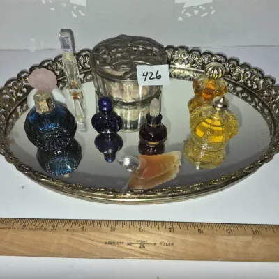 Sale Photo Thumbnail #744: Collection of vintage miniature perfume bottles and a trinket box displayed on an ornate silver-tone mirrored vanity tray.