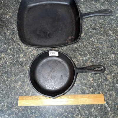 Sale Photo Thumbnail #648: Two vintage cast iron skillets, including one large square griddle and one small round skillet, shown with a ruler for scale.