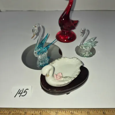 Sale Photo Thumbnail #246: Collection of four vintage bird figurines, including a tall red glass swan, two spun glass swans on mirror bases, and a porcelain swan trinket dish with applied pink rose accent on a wooden base.