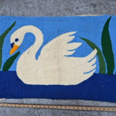 Sale Photo Thumbnail #185: Hand-hooked yarn rug depicting a white swan floating on blue water among green reeds, measuring approximately 35 inches wide.
