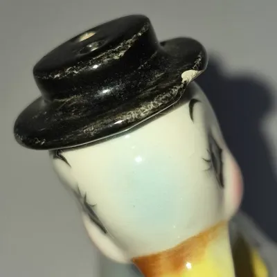 Sale Photo Thumbnail #219: Vintage ceramic duck-shaped salt shaker featuring a black hat, with visible wear and a small chip on the brim.
