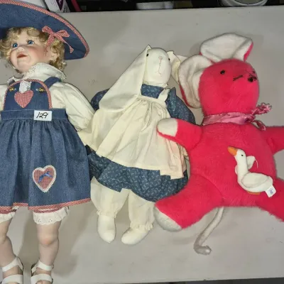 Sale Photo Thumbnail #210: Collection of vintage dolls and plush toys, including a porcelain girl doll in denim overalls, a handmade cloth bunny doll, and a bright pink stuffed mouse.