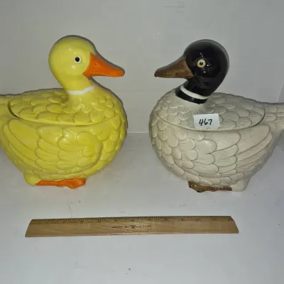 Sale Photo Thumbnail #804: Pair of vintage ceramic duck cookie jars, featuring one bright yellow duck and one mallard with a black head, displayed alongside a wooden ruler for scale.