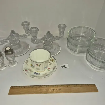 Sale Photo Thumbnail #416: Assortment of glassware and china including double candelabras, glass salt and pepper shakers, nested glass bowls, and a floral teacup with saucer.